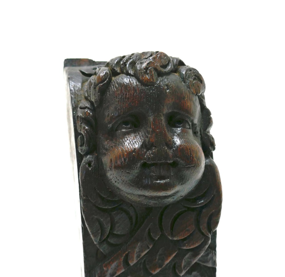 A dark carved oak architectural applique featuring a sculpted cherub head with folded wings and a fan motif at the base. View IV
