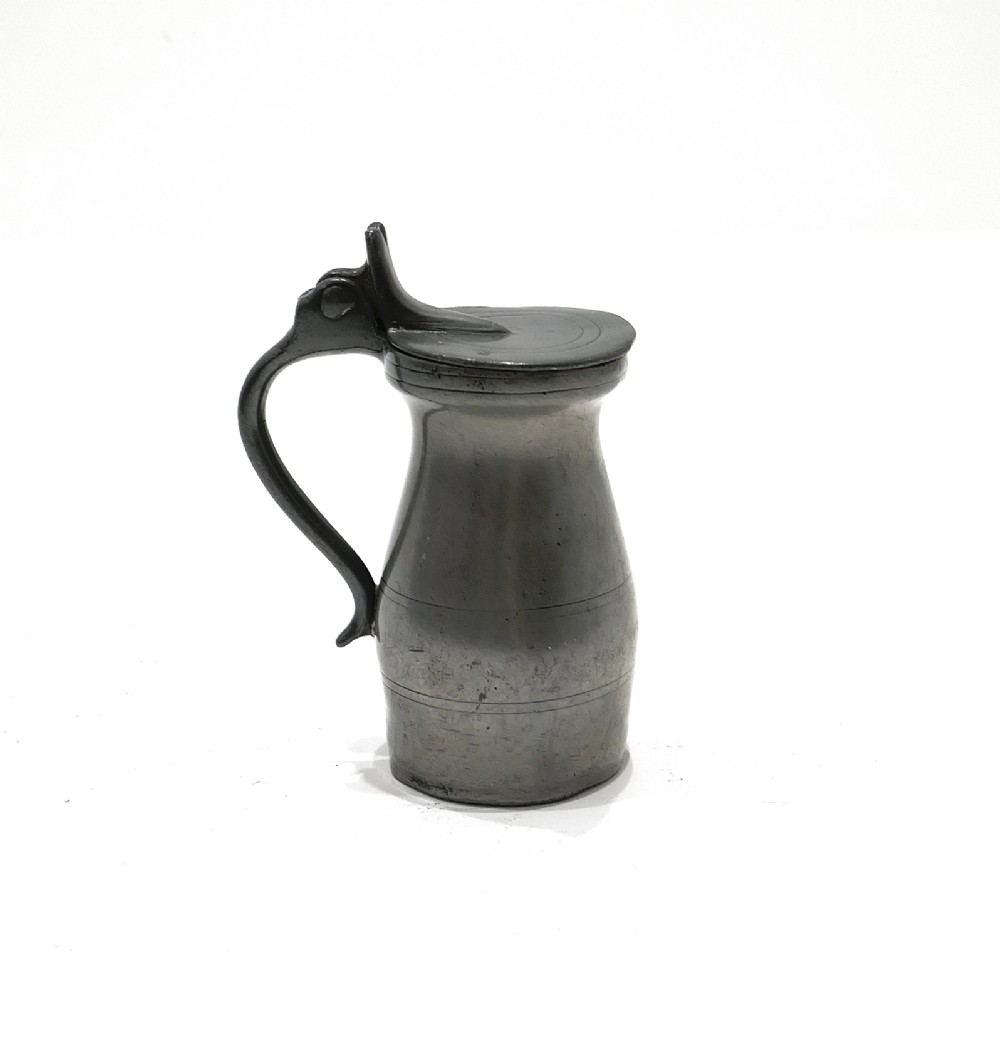 An 18th-century English pewter spirit measure featuring a flat hinged lid, curved handle, and incised horizontal lines around a baluster body.
