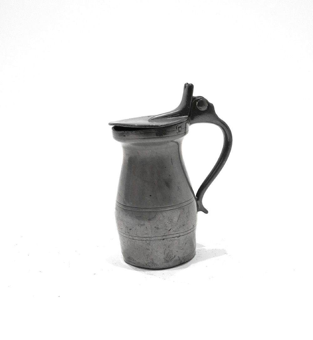 An 18th-century English pewter spirit measure featuring a flat hinged lid, curved handle, and incised horizontal lines around a baluster body. View II