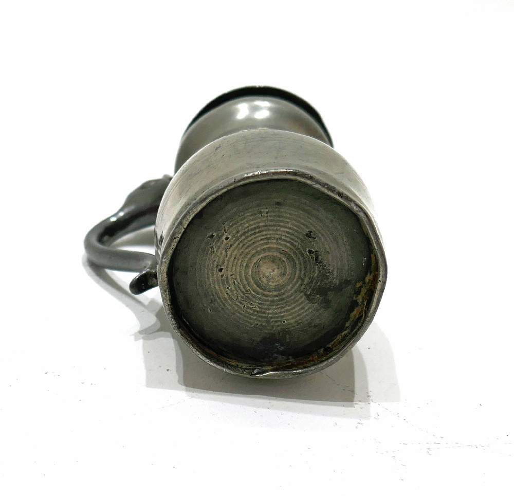An 18th-century English pewter spirit measure featuring a flat hinged lid, curved handle, and incised horizontal lines around a baluster body. View V