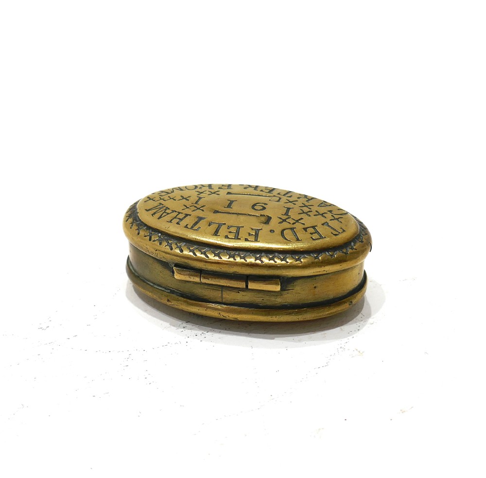 An oval brass snuff box featuring hand-engraved text that reads Ted Feltham 1911 Carter Frome surrounded by small hammer motifs and decorative border crosshatching. View III