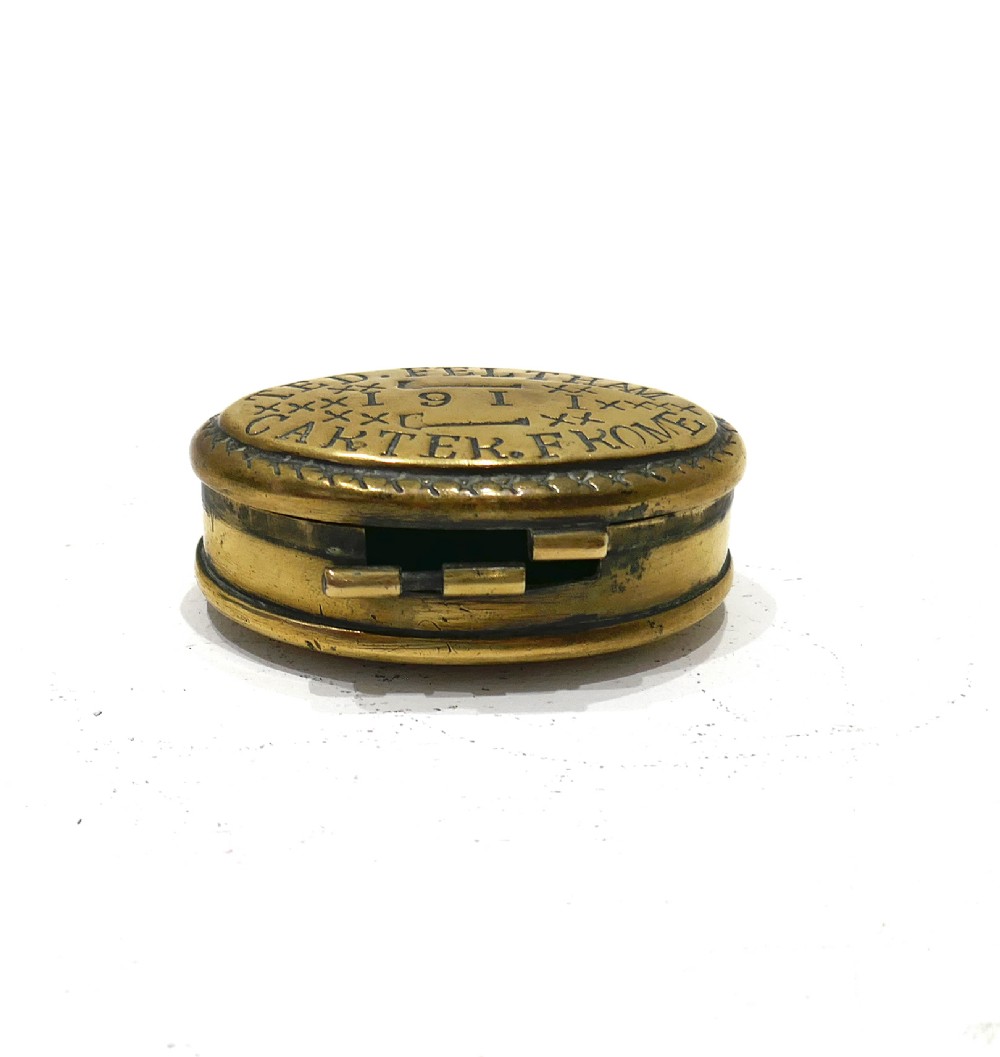 An oval brass snuff box featuring hand-engraved text that reads Ted Feltham 1911 Carter Frome surrounded by small hammer motifs and decorative border crosshatching. View IV