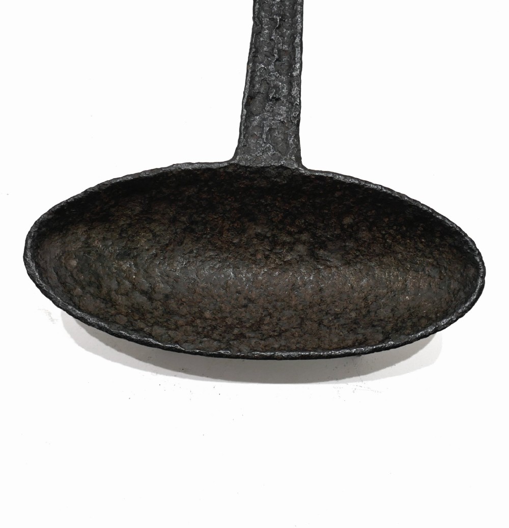A 17th-century cast iron hearth grisset featuring a shallow boat-shaped vessel with three short tripod feet and a straight handle against a white backdrop. View IV