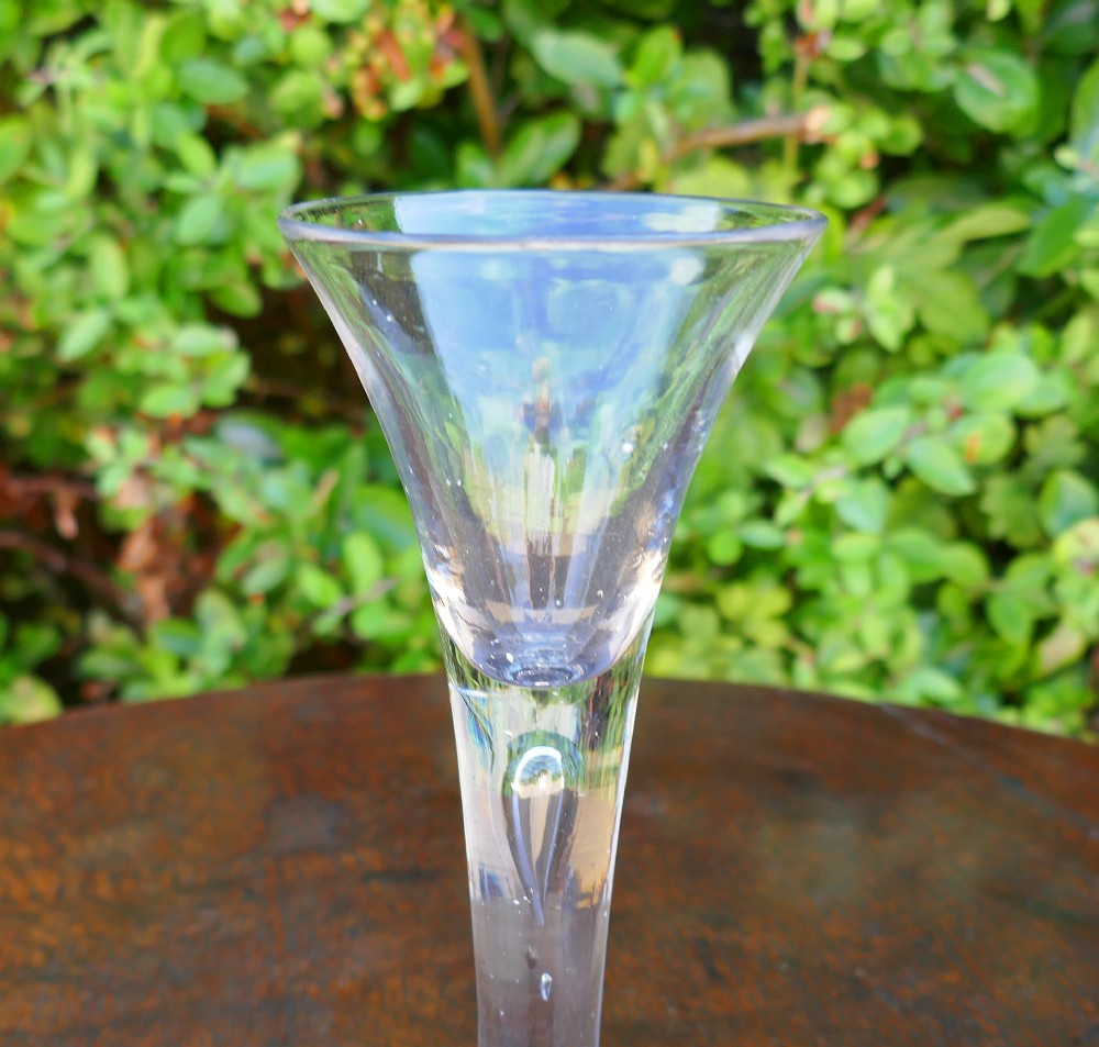 An 18th-century clear hand-blown glass wine goblet with a trumpet bowl, a drawn stem featuring a central teardrop air bubble, and a flat conical base. View III