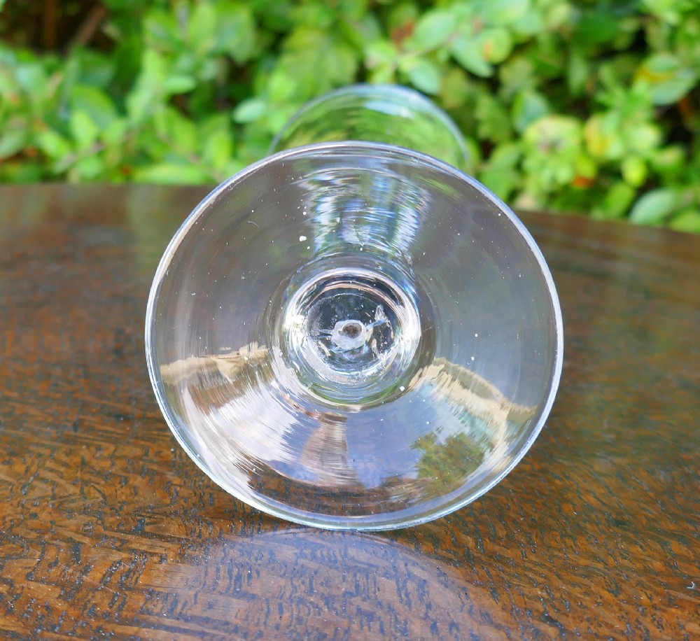 An 18th-century clear hand-blown glass wine goblet with a trumpet bowl, a drawn stem featuring a central teardrop air bubble, and a flat conical base. View IV