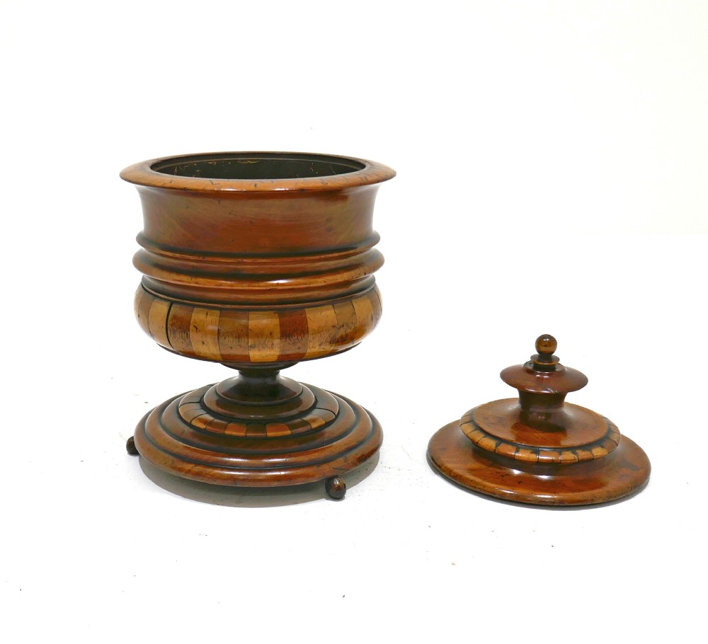 A turned antique wooden lidded tobacco jar with staved bands of light and dark timber, set on a pedestal base with small ball feet. View II