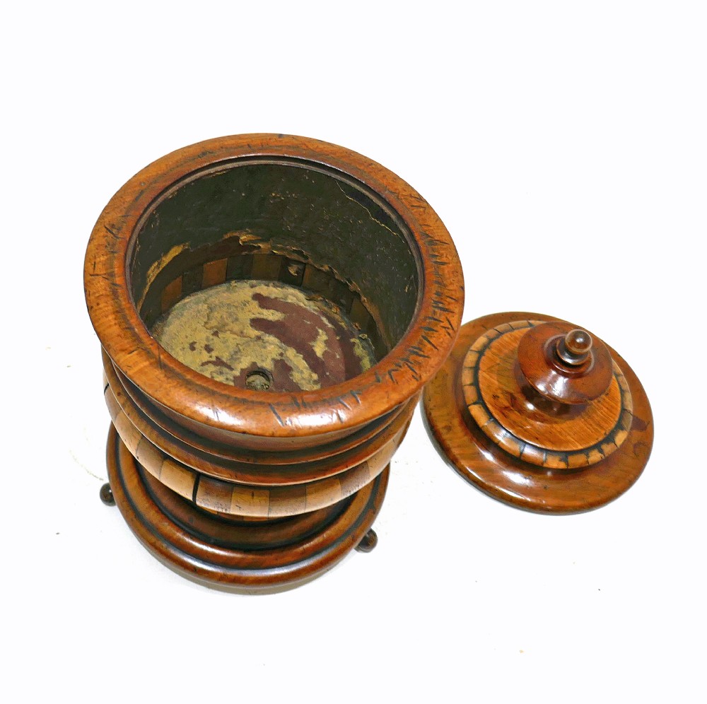 A turned antique wooden lidded tobacco jar with staved bands of light and dark timber, set on a pedestal base with small ball feet. View IV