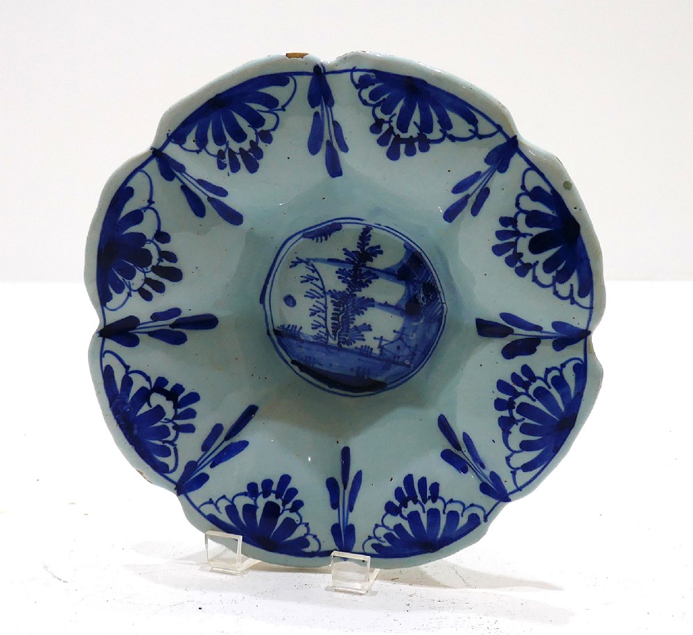 An antique 17th-century English tin-glazed earthenware lobed dish featuring hand-painted cobalt blue floral panels and a central landscape scene.