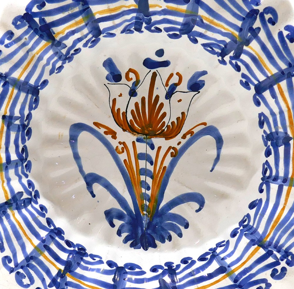 A 17th-century Dutch Delftware lobed ceramic dish featuring a central tulip motif surrounded by blue and yellow hand-painted patterns on an off-white background. View II