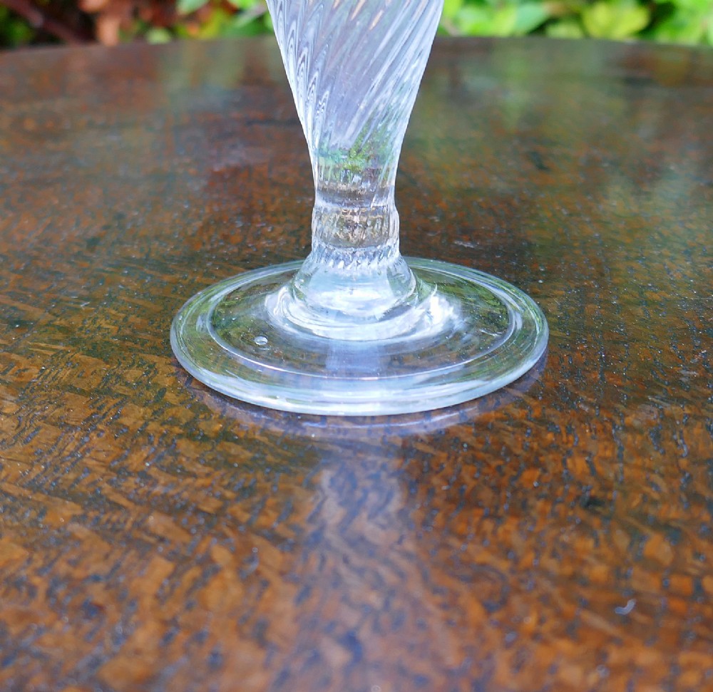 An 18th-century clear glass ale glass featuring spiral wrythen fluting on a conical bowl and a circular folded foot. View II