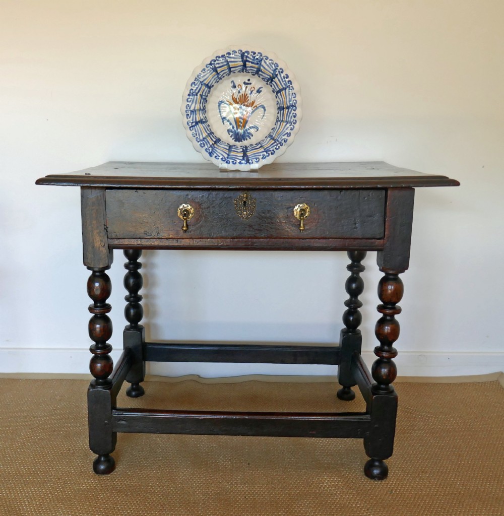 A 17th-century English oak side table featuring a single drawer with brass drop handles, turned ball legs, and a perimeter stretcher base.