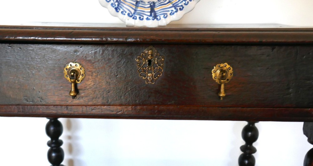 A 17th-century English oak side table featuring a single drawer with brass drop handles, turned ball legs, and a perimeter stretcher base. View II