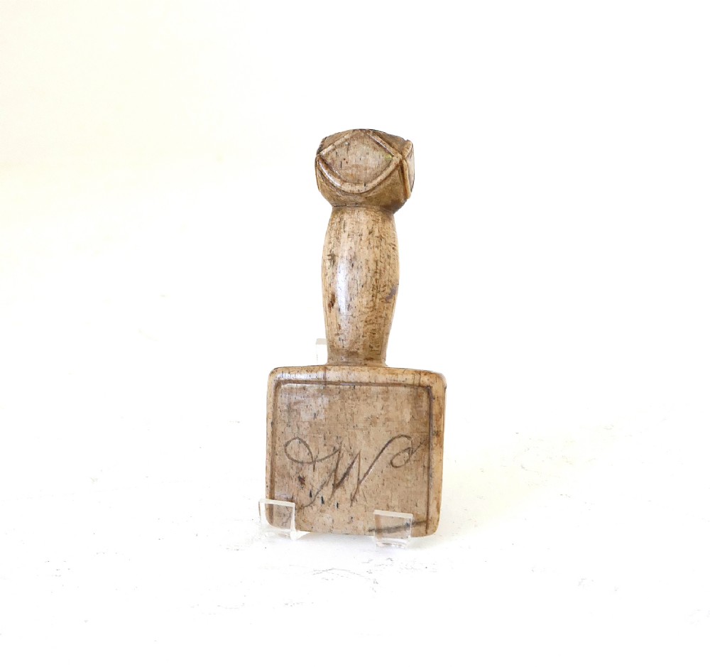 A carved 19th-century whalebone seam rubber featuring a decorative geometric handle and initialled lettering on the flat blade face.