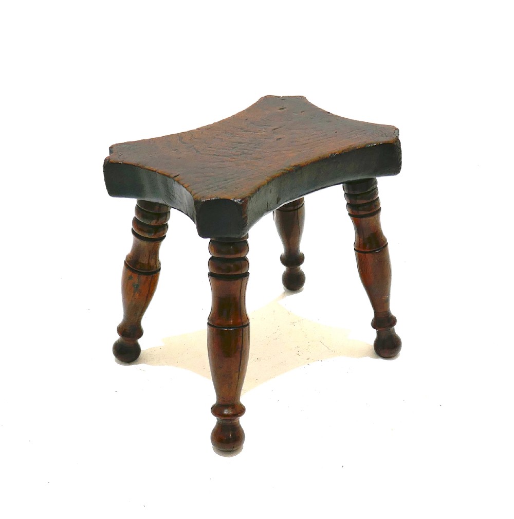 A nineteenth-century dark ash and elm lacemakers stool featuring a thick contoured rectangular seat and four turned wood legs. View II