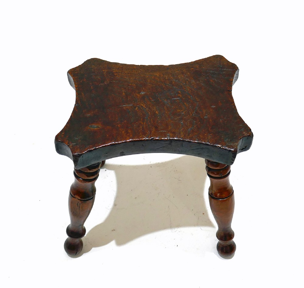 A nineteenth-century dark ash and elm lacemakers stool featuring a thick contoured rectangular seat and four turned wood legs. View IV