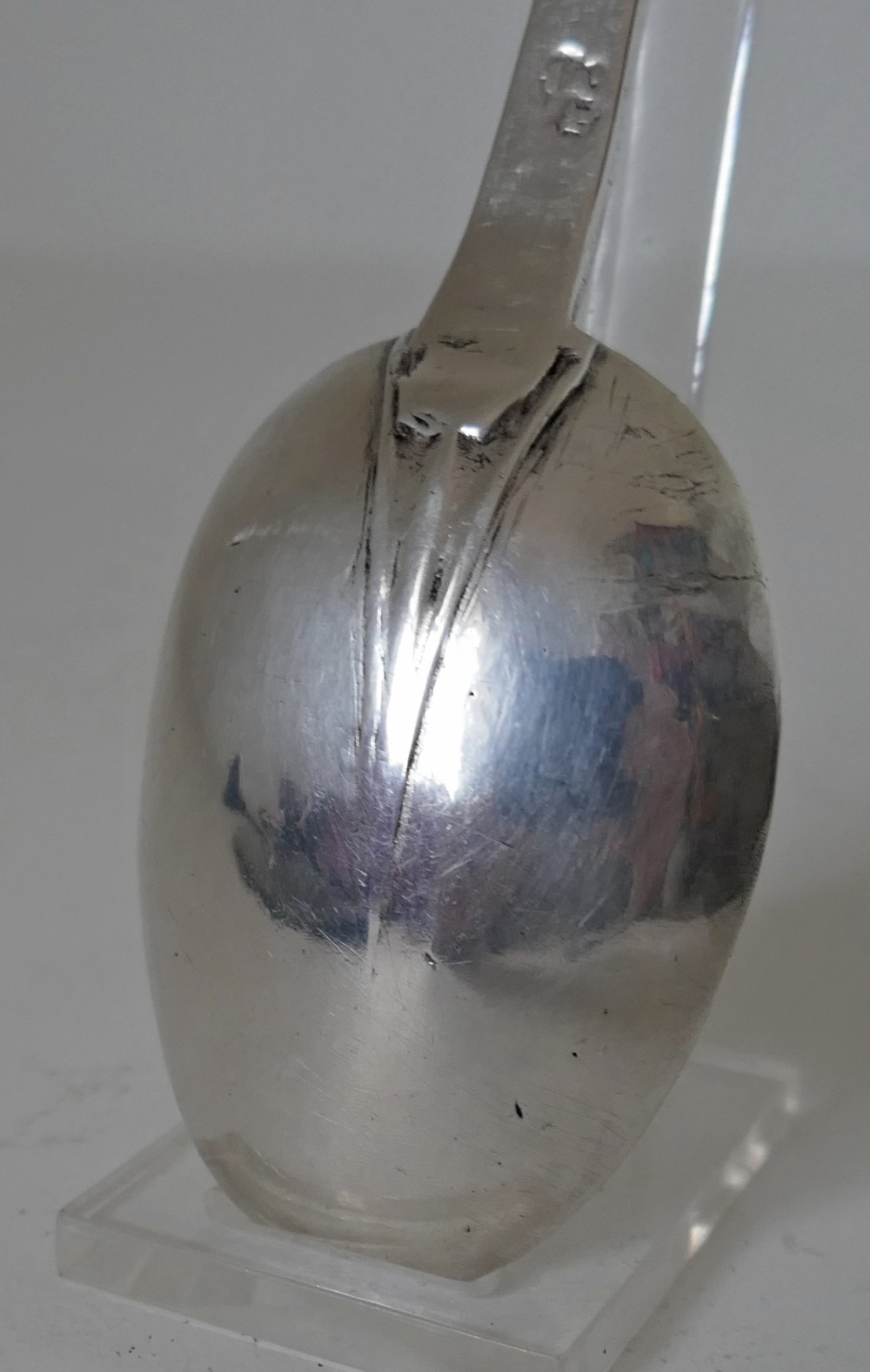 A 17th-century English sterling silver trefid spoon with a lobed terminal handle and an oval bowl displayed on a clear stand. View V