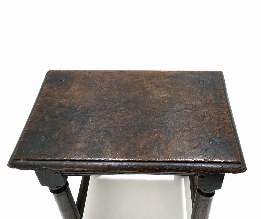 A 17th-century Commonwealth joined oak stool featuring turned legs, pegged mortise joints, lower stretchers, and a moulded rectangular seat. View III