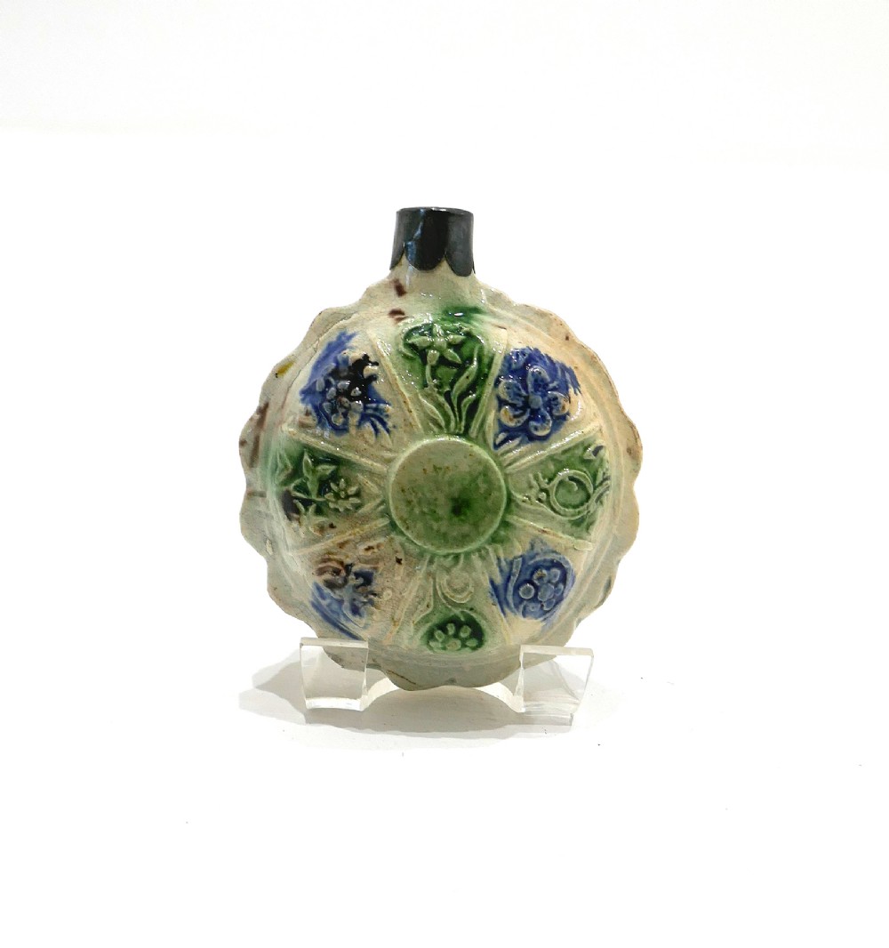 An 18th-century circular ceramic spirit flask featuring relief-moulded floral panels glazed in green, blue, and brown hues on a light cream earthenware body.