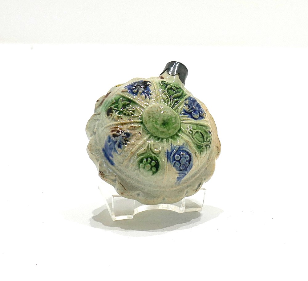 An 18th-century circular ceramic spirit flask featuring relief-moulded floral panels glazed in green, blue, and brown hues on a light cream earthenware body. View III