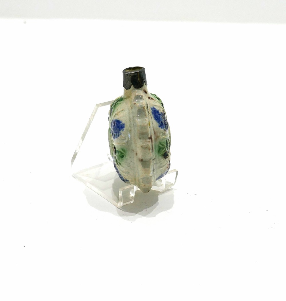 An 18th-century circular ceramic spirit flask featuring relief-moulded floral panels glazed in green, blue, and brown hues on a light cream earthenware body. View IV