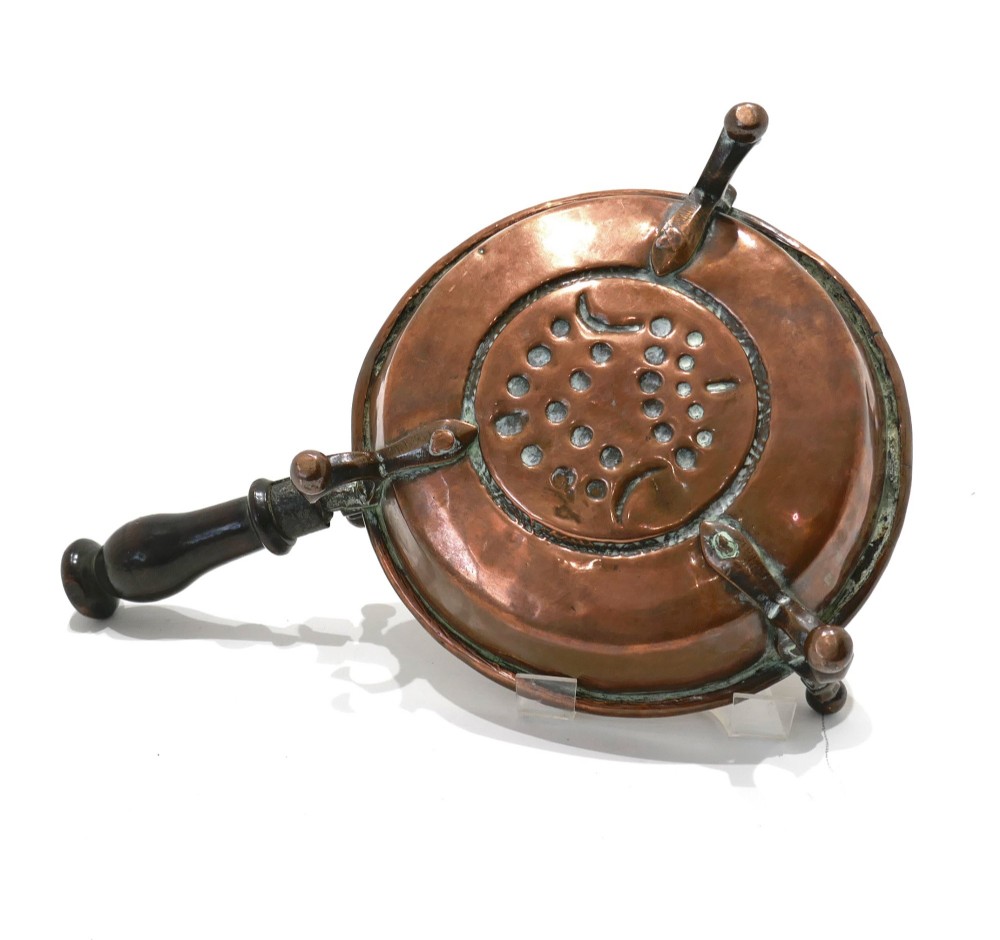 An antique Dutch copper brazier featuring a central repousse motif, a turned fruitwood handle, and three upright rim pegs. View II