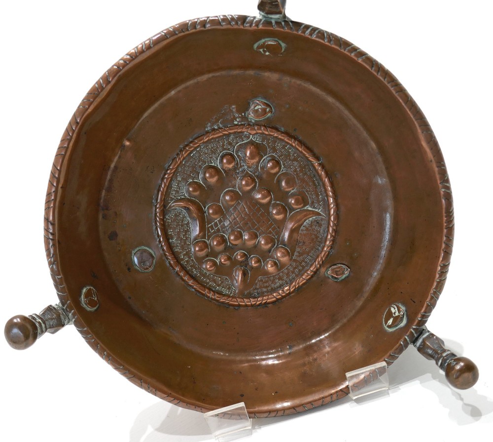 An antique Dutch copper brazier featuring a central repousse motif, a turned fruitwood handle, and three upright rim pegs. View V