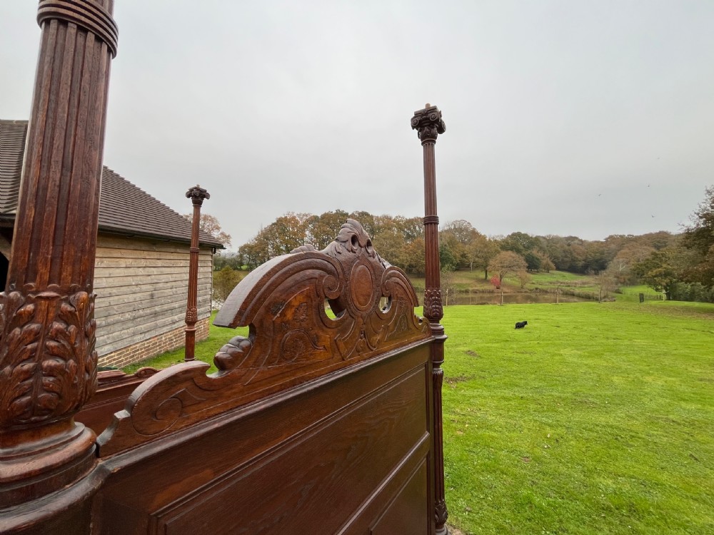 A dark carved oak four poster bed featuring turned columns, an ornate carved headboard, and a gold fabric-lined canopy. View II