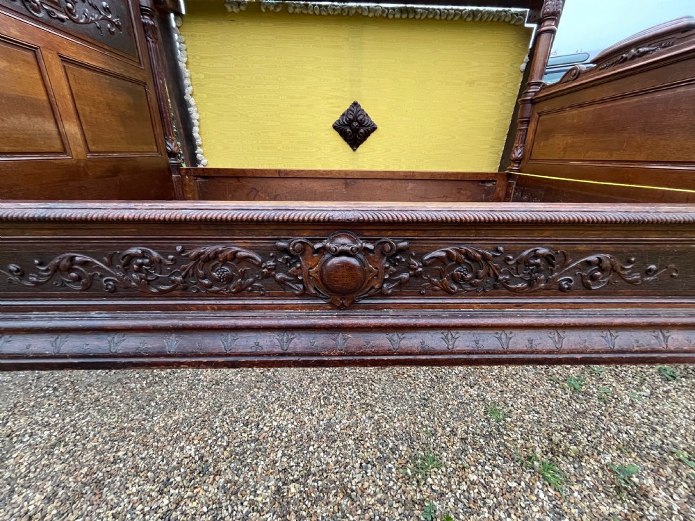 A dark carved oak four poster bed featuring turned columns, an ornate carved headboard, and a gold fabric-lined canopy. View V
