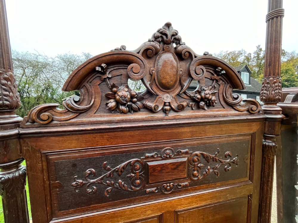 A dark carved oak four poster bed featuring turned columns, an ornate carved headboard, and a gold fabric-lined canopy. View VI
