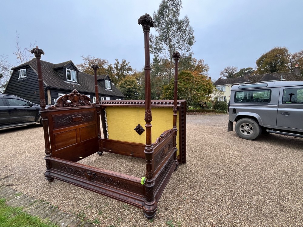 A dark carved oak four poster bed featuring turned columns, an ornate carved headboard, and a gold fabric-lined canopy. View IX