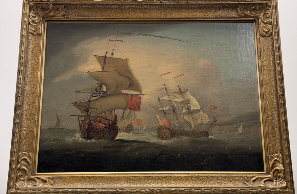 An 18th-century marine oil painting depicting warships at sea with raised sails and flags, set within an ornate gilded wood frame.