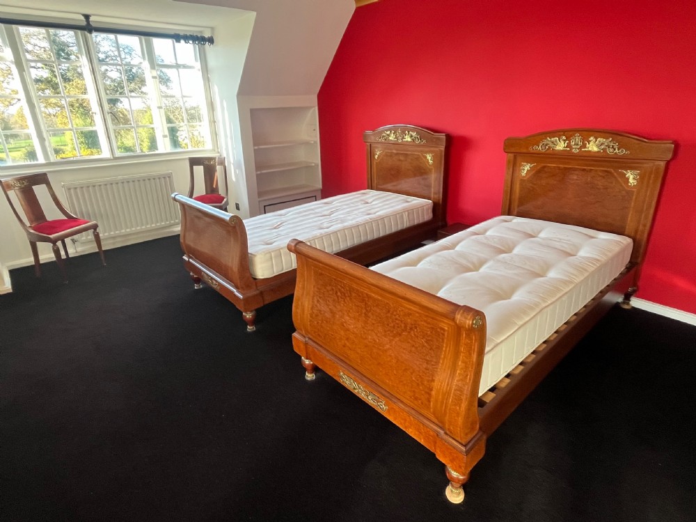 A pair of late nineteenth-century French Empire single sleigh beds crafted from warm brown polished wood with ornamental gilt mounts on the headboards and footboards.