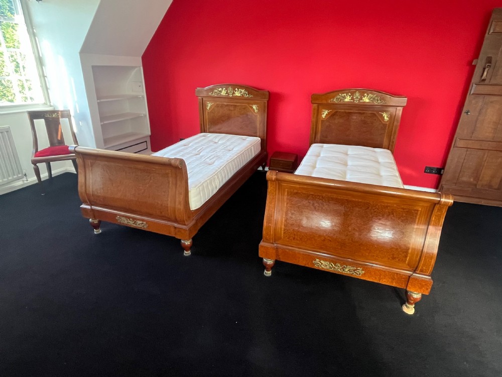 A pair of late nineteenth-century French Empire single sleigh beds crafted from warm brown polished wood with ornamental gilt mounts on the headboards and footboards. View V
