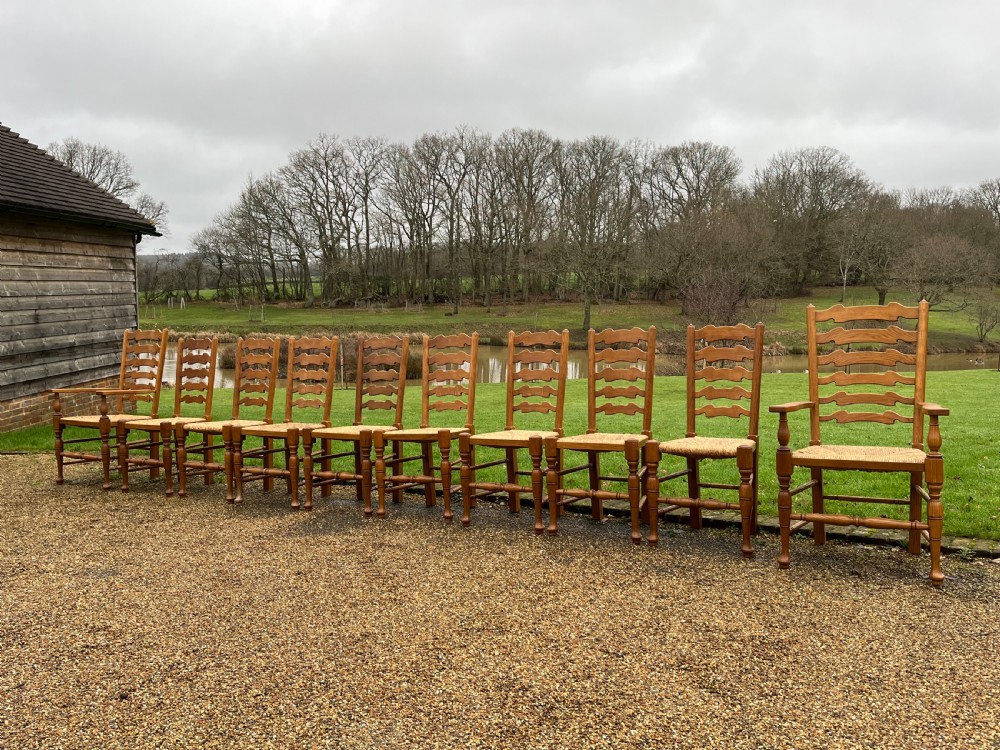 A set of ten antique oak ladder back dining chairs featuring woven rush seats and turned legs, comprising eight side chairs and two carver armchairs.