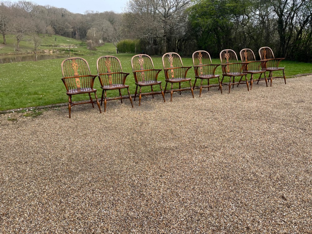 A set of eight matching wooden Windsor armchairs featuring pierced splats, turned spindles, curved armrests, and turned legs.