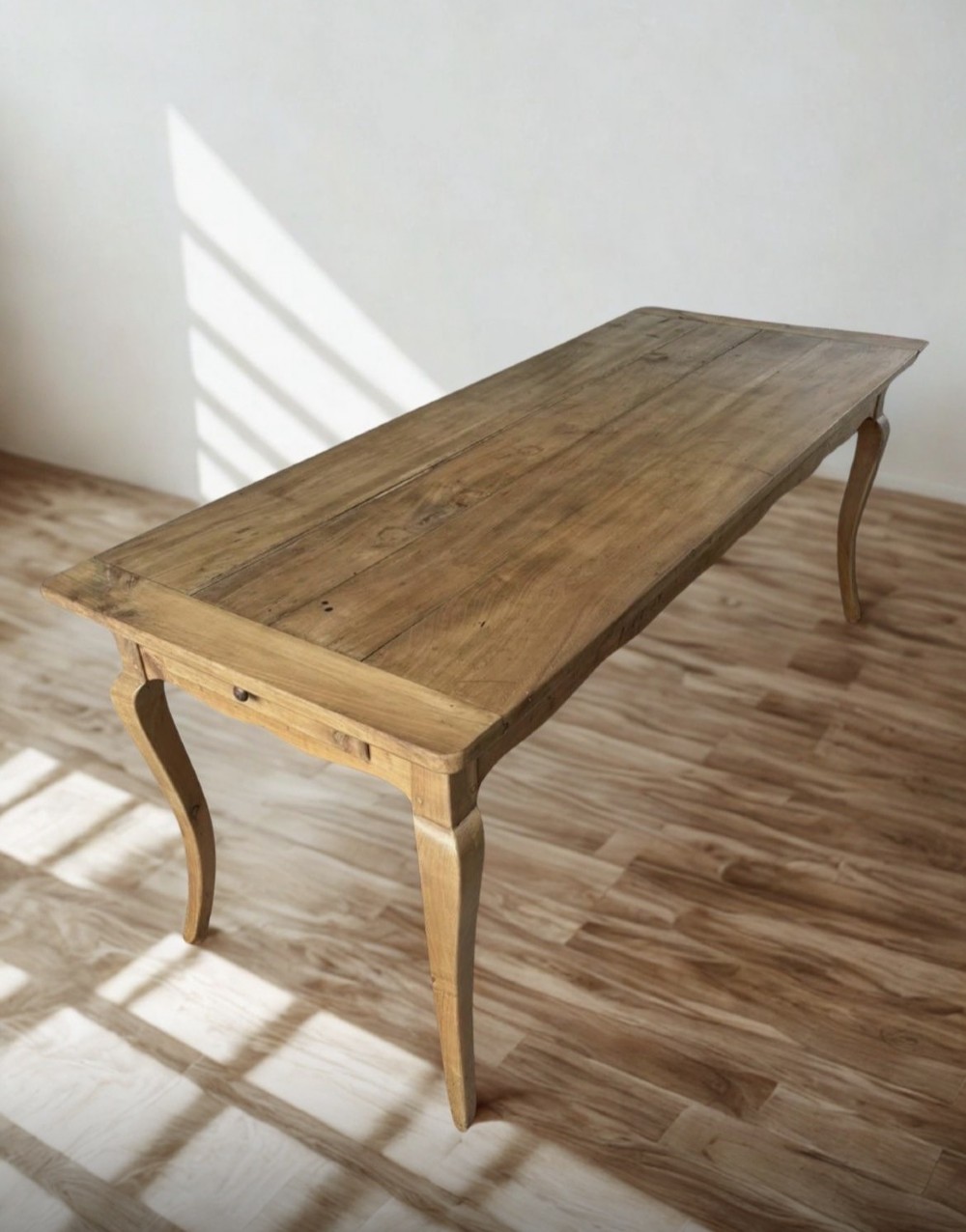 A late nineteenth-century French cherrywood dining table featuring curved cabriolet legs, a planked top, and an apron drawer.