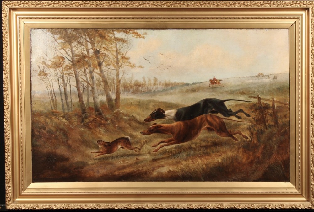 A nineteenth-century oil painting on canvas depicting two greyhounds in full motion chasing a hare across a grassy landscape within a carved gilt frame.