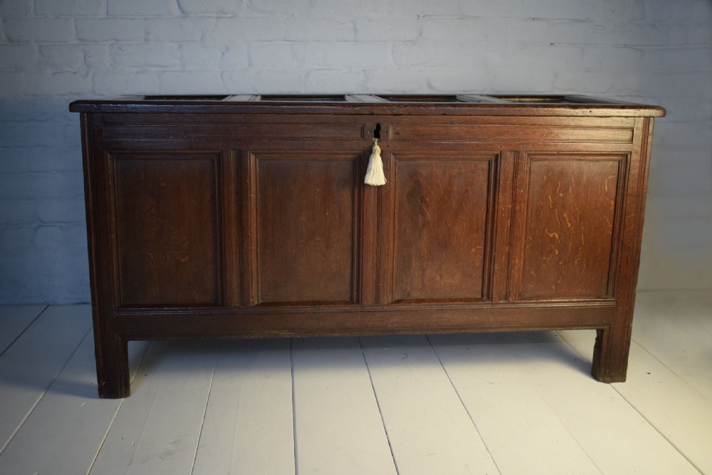 A dark oak panelled storage coffer with four inset front panels, a flat hinged lid, and sturdy stile feet.