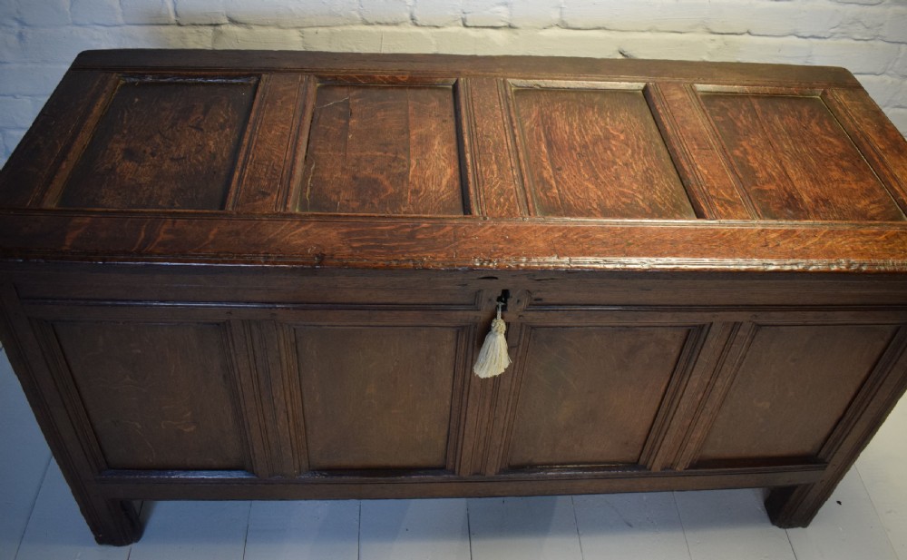 A dark oak panelled storage coffer with four inset front panels, a flat hinged lid, and sturdy stile feet. View II