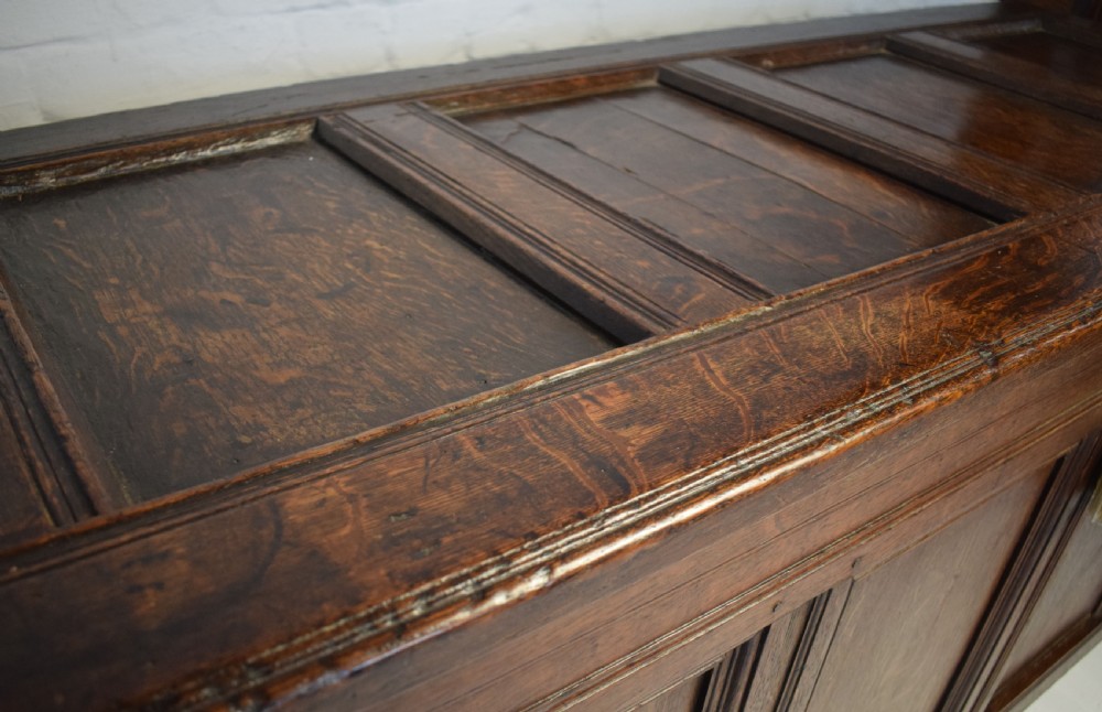 A dark oak panelled storage coffer with four inset front panels, a flat hinged lid, and sturdy stile feet. View VII