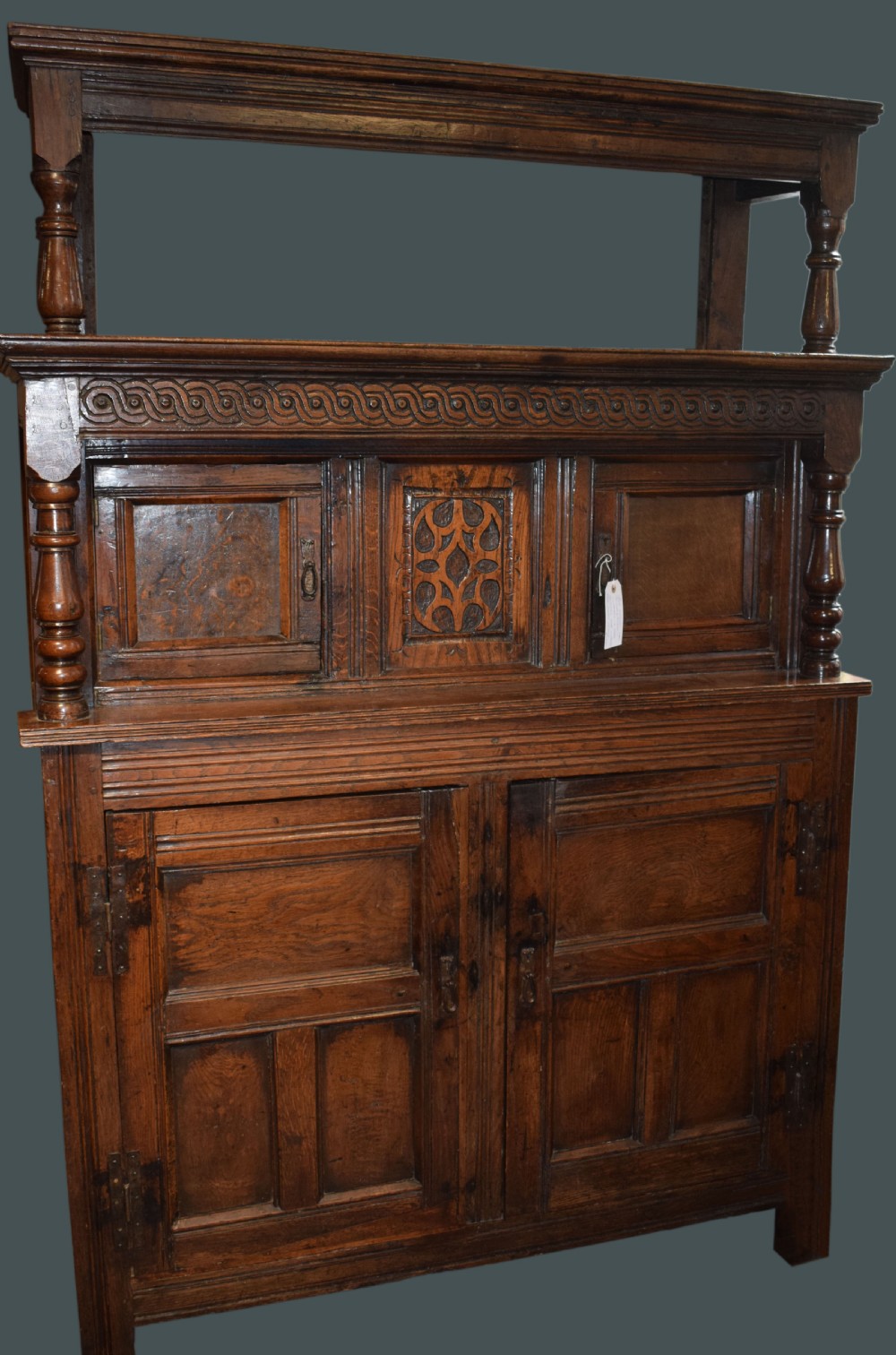 A three-tier dark oak Welsh tridarn dresser featuring carved frieze panels, baluster supports, and lower cupboard doors.