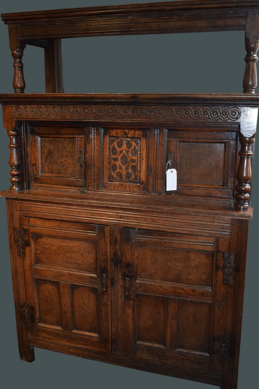 A three-tier dark oak Welsh tridarn dresser featuring carved frieze panels, baluster supports, and lower cupboard doors. View II