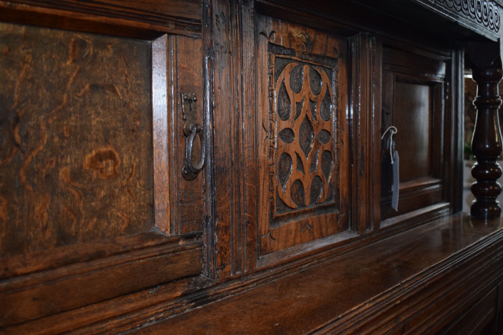 A three-tier dark oak Welsh tridarn dresser featuring carved frieze panels, baluster supports, and lower cupboard doors. View VII