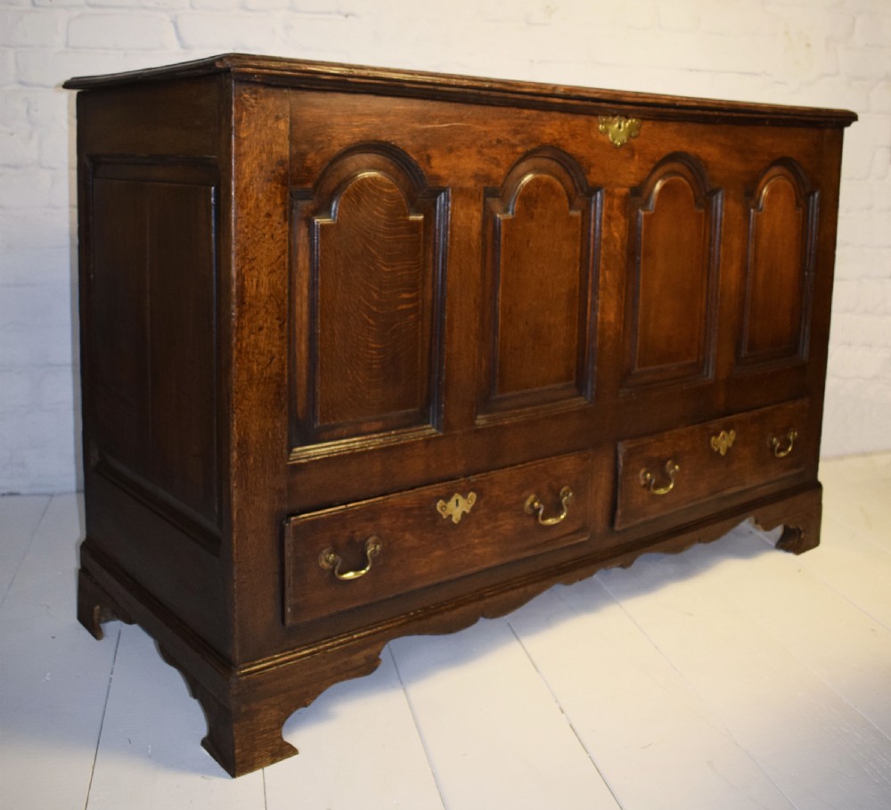 A dark oak antique mule chest featuring four arched fielded panels, two lower drawers with brass drop handles, and bracket feet. View X