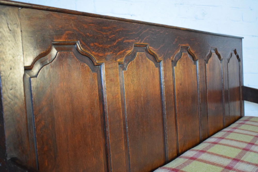 A dark oak Georgian settle featuring a five-panel fielded backrest, shaped armrests, turned legs, and a check pattern seat cushion. View II