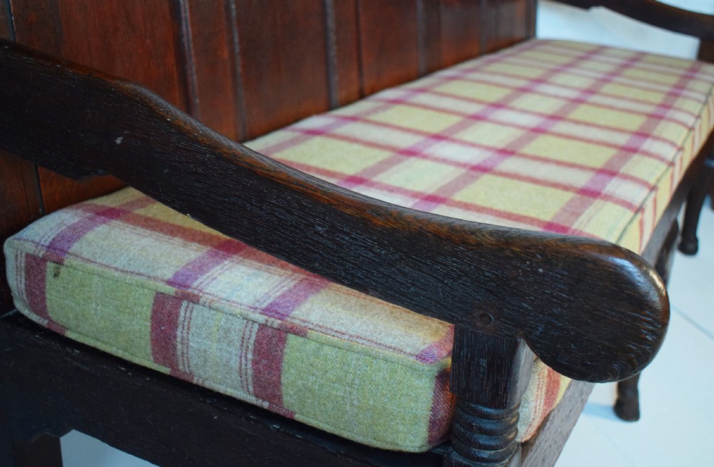 A dark oak Georgian settle featuring a five-panel fielded backrest, shaped armrests, turned legs, and a check pattern seat cushion. View III