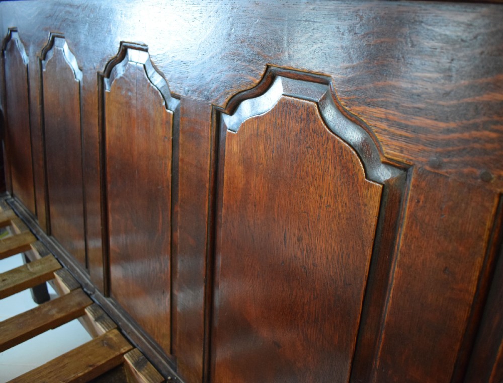 A dark oak Georgian settle featuring a five-panel fielded backrest, shaped armrests, turned legs, and a check pattern seat cushion. View V