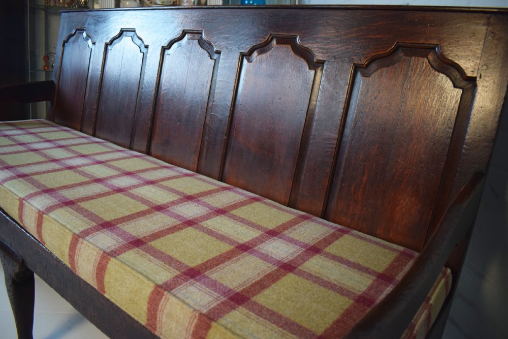 A dark oak Georgian settle featuring a five-panel fielded backrest, shaped armrests, turned legs, and a check pattern seat cushion. View VI