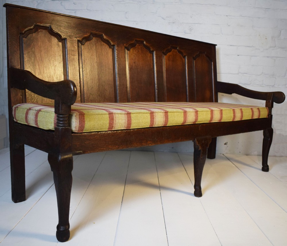 A dark oak Georgian settle featuring a five-panel fielded backrest, shaped armrests, turned legs, and a check pattern seat cushion. View VIII