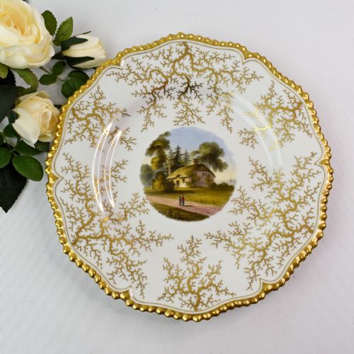 fig 1. A Regency porcelain dessert plate featuring a hand-painted central landscape surrounded by intricate gold gilt seaweed patterns on a scalloped white border.